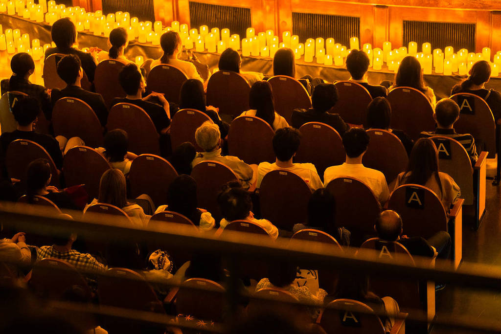 Plano generald e muchos espectadores mirando atentos hacia un escenairo cubierto de velas durante un concierto Candlelight.