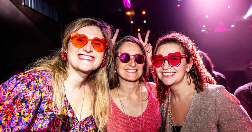 Primer plano de tres chicas vestidas de disco sonriendo a cámara durante Gimme Gimme Disco.