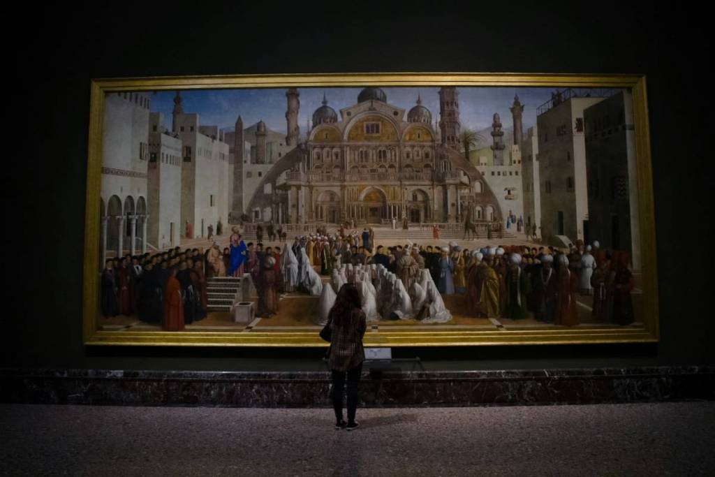 Una visitatrice di spalle osserva la monumentale tela "Predica di san Marco in una piazza di Alessandria d'Egitto" di Gentile e Giovanni Bellini all'interno della Pinacoteca di Brera di Milano.