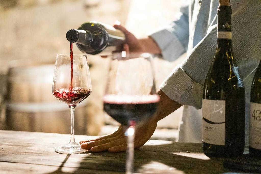 A waiter pours red wine into two glasses.