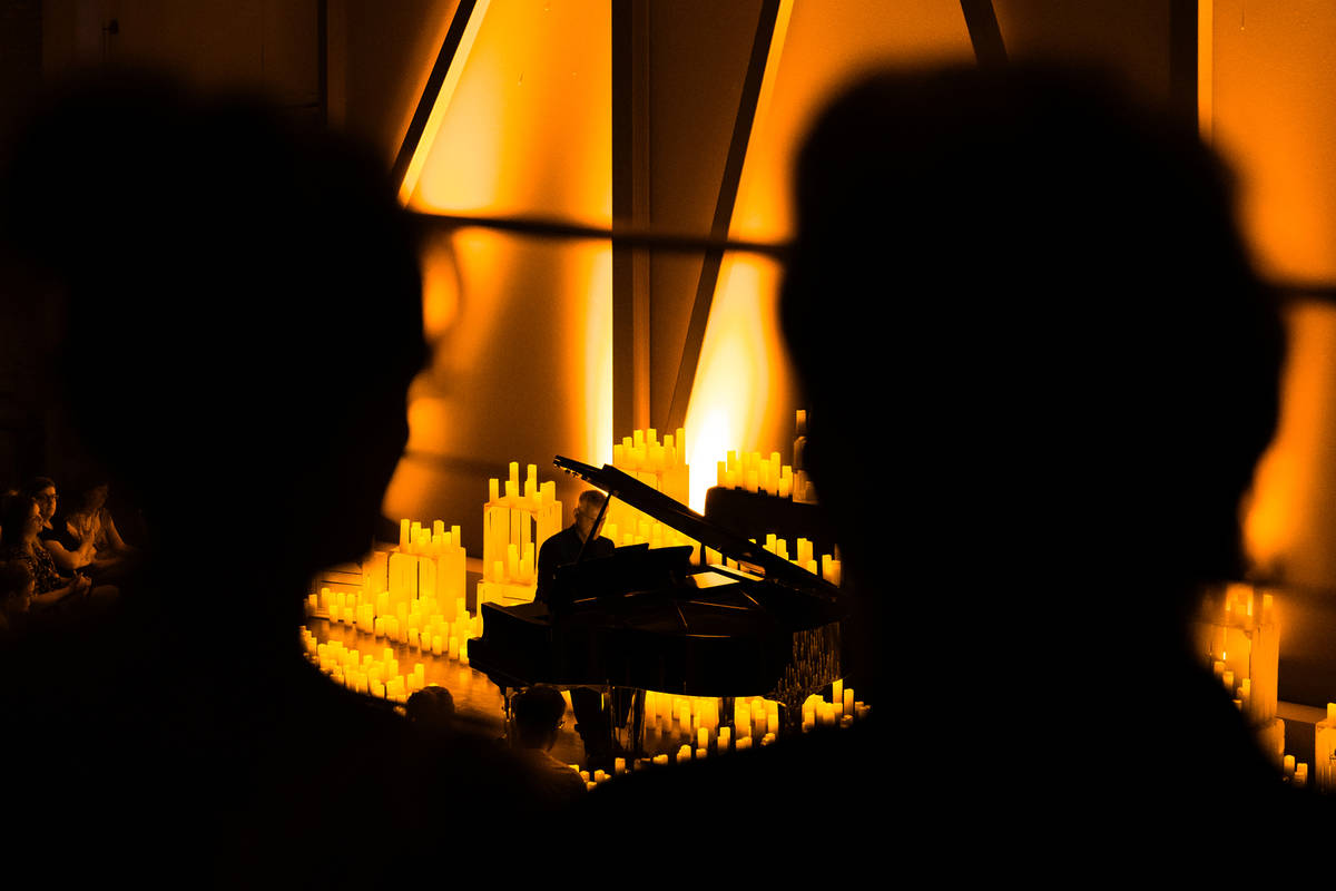 Photo de deux personnes à contre jour en premier plan assistant à un concert Candlelight et d'un pianiste au milieu