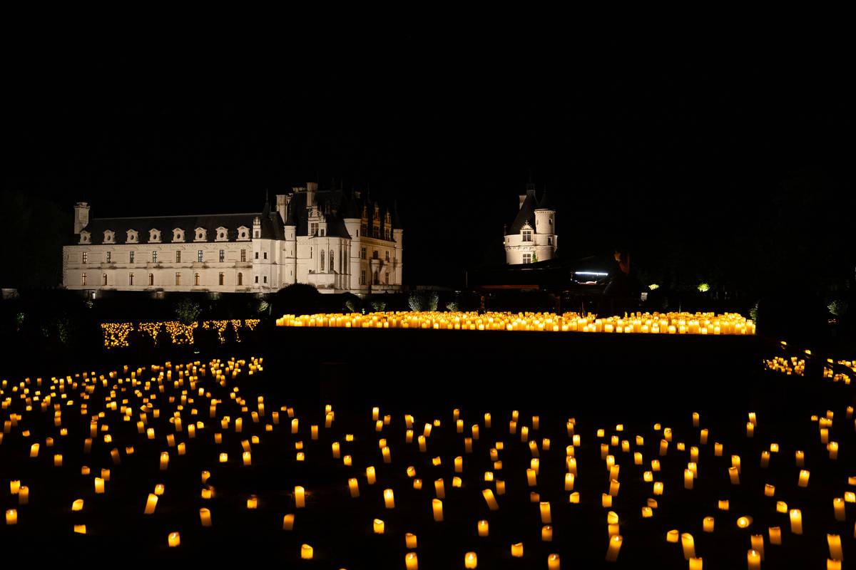 Photo d'une scène avec un piano entourée de milliers de bougies avec un chateau en fond