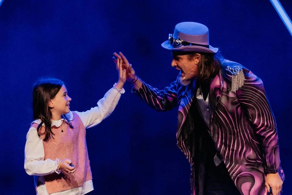 Un magicien tape dans la main d'un enfant sur scène à The Magic Gateway.