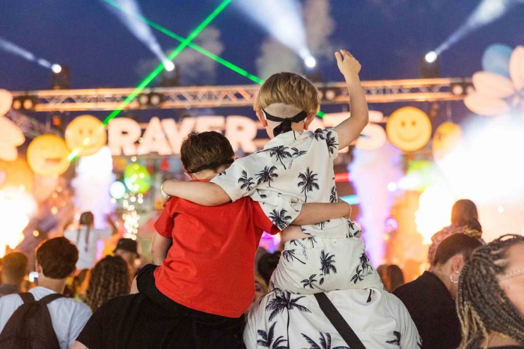 Foto di due bambini sulle spalle dei genitori, che ballano al Raver Tots