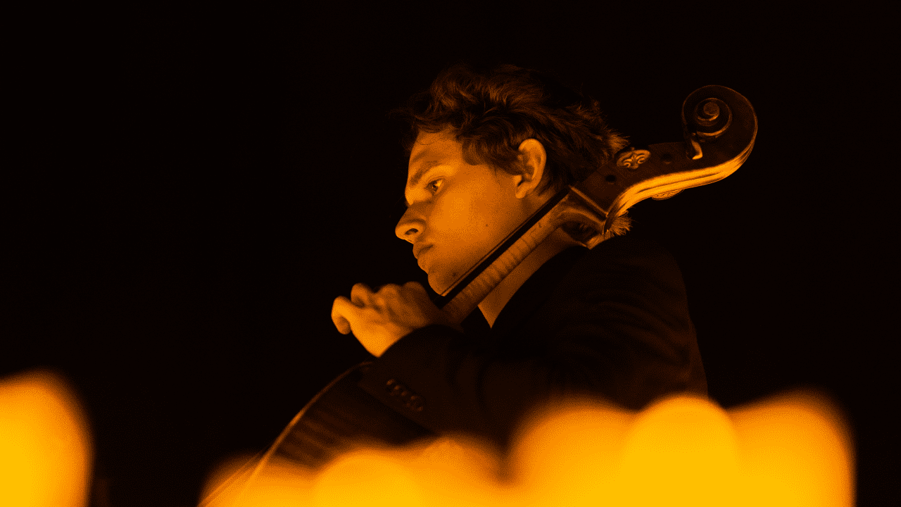 Photo d'un violoncellliste en plein concert illuminé par les bougies