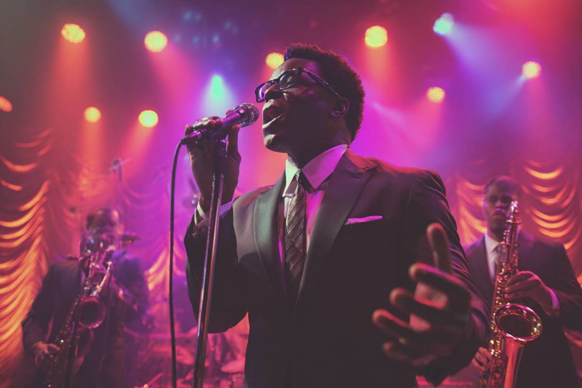 homem cantando em palco com luzes vermelhas e lilás no The Jazz Room: Tributo ao Blues