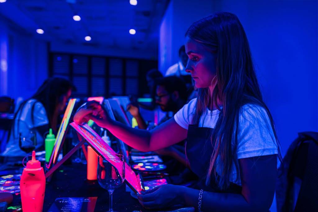 A woman painting under neon lights at a Neon Brush workshop.