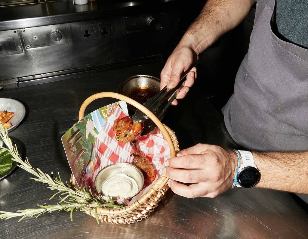 A hand loads fast food into a basket which already contains a creamy dip