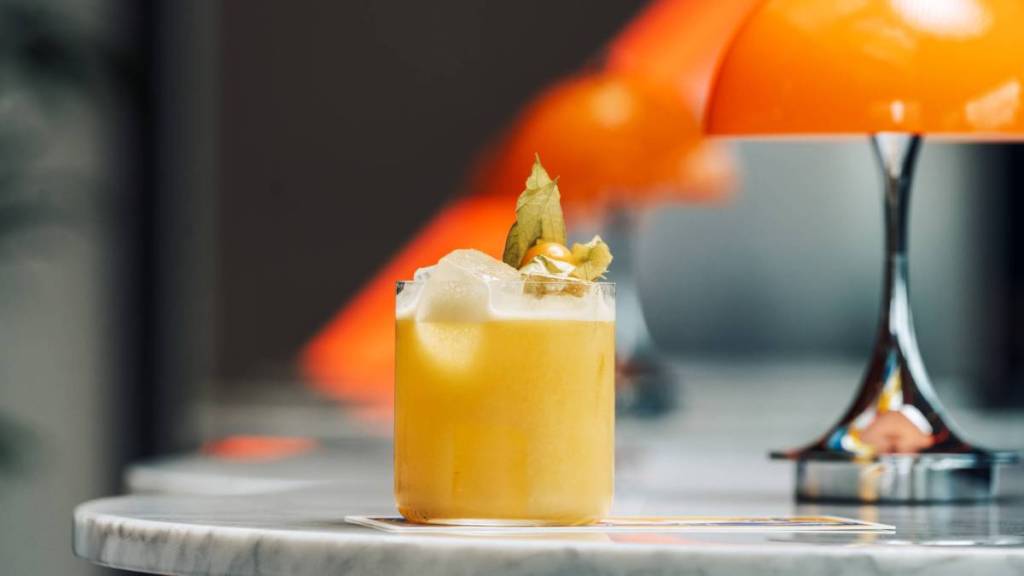 A cocktail on a marble table with orange table lamps behind it