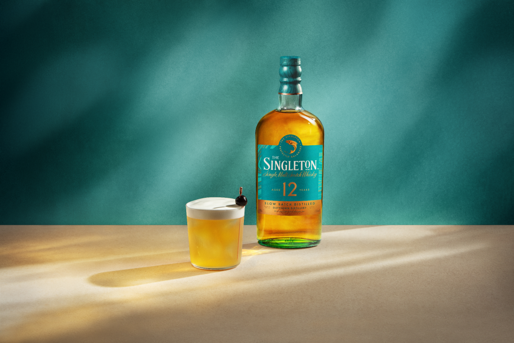 A bottle of Singleton whisky and a cocktail in front of a green background