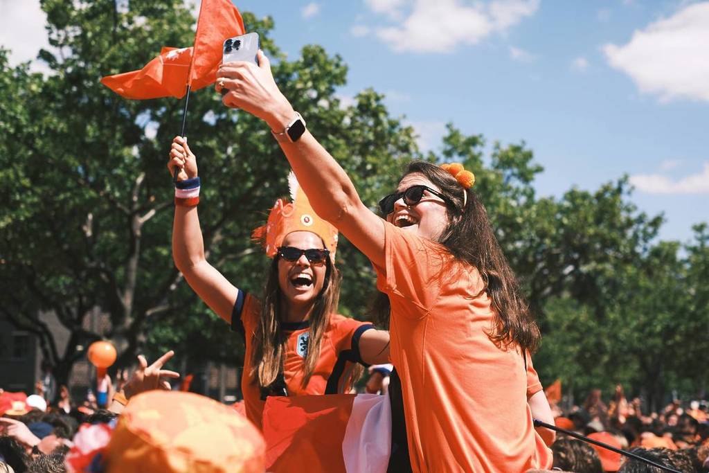 Two smiling girls in Dutch jerseys enthusiastically celebrating and having fun.