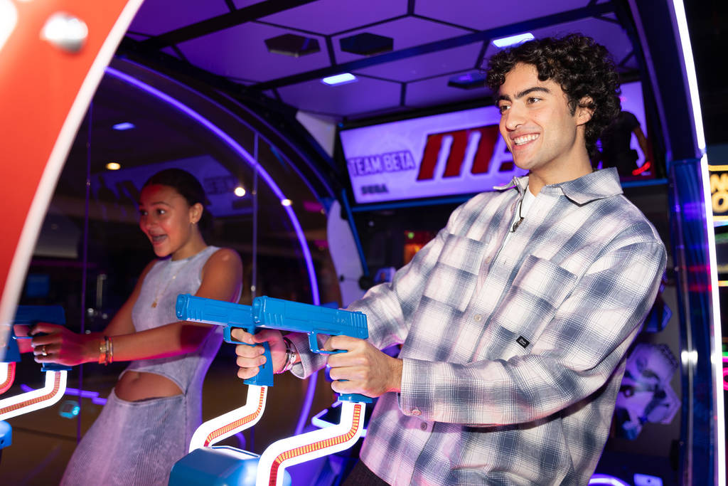 Man and woman playing a shooter game in a neon-lit arcade