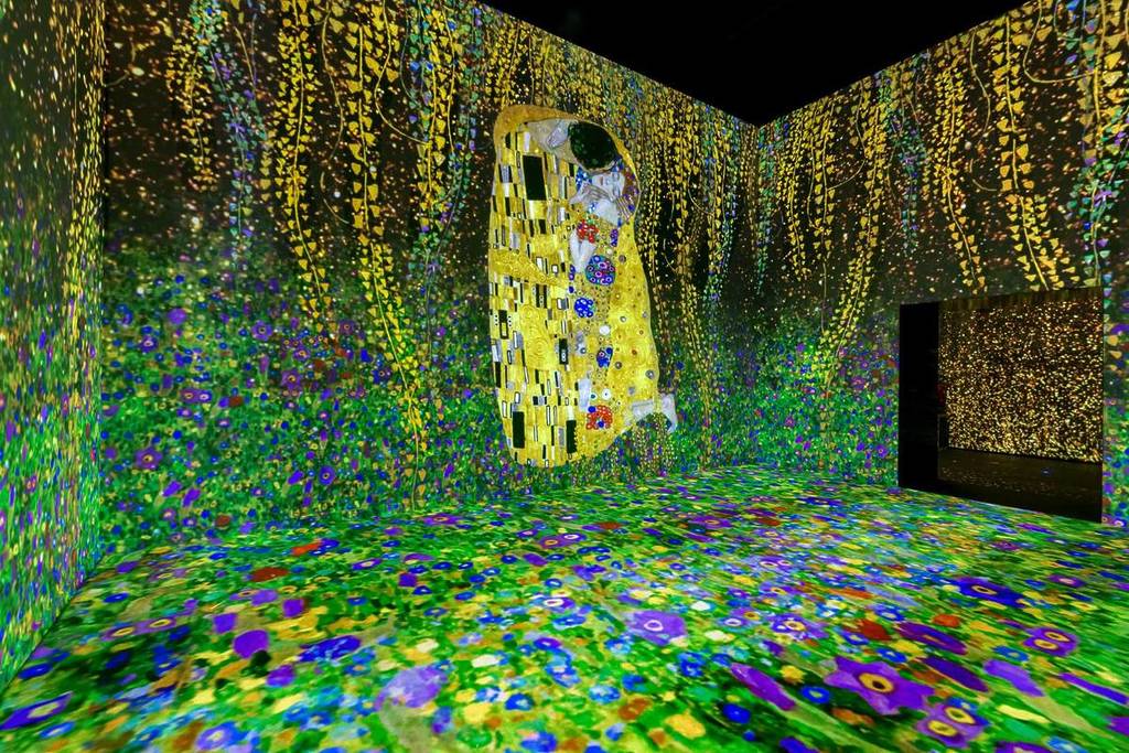 Proiezione digitale de “Il bacio” di Gustav Klimt in uno spazio le cui pareti e il pavimento sono interamente ricoperti da un mare di fiori colorati e luminosi.
