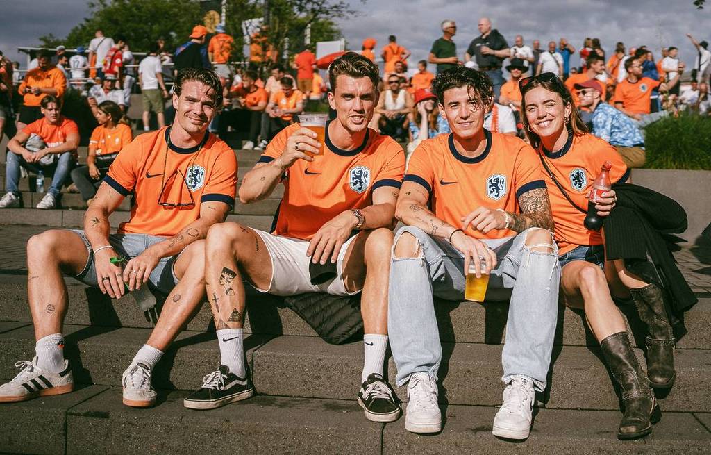 Un gruppo di amici con la maglia arancione della Nazionale olandese si gode l'atmosfera all'aperto con una birra e una bibita durante i Mondiali di calcio.