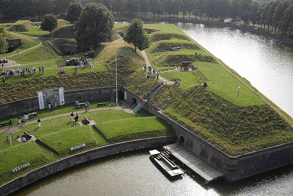 Vista dall'alto del Bastione Turfpoort con la parte all'aperto del Museo della Fortezza, i cannoni storici sui bastioni erbosi e un pontile di legno con una barca nel fossato della fortezza.