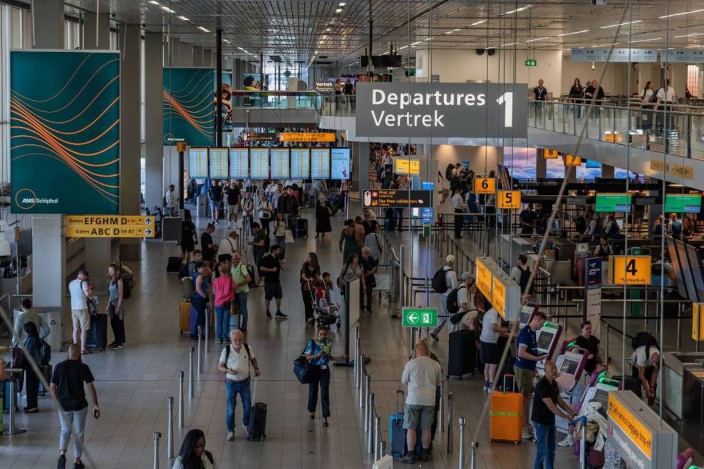 A view of a busy airport departure hall where travelers are standing in line with their luggage at the check-in counters.