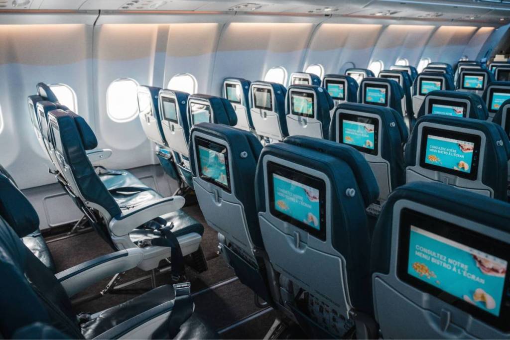 Interior of an empty passenger plane with rows of blue seats and built-in entertainment screens in the seatbacks.