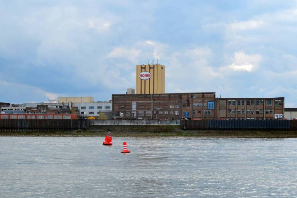 The Honig Complex in Nijmegen, featuring the iconic yellow factory tower of the former soup factory, as seen from across the Waal River with red buoys in the water.