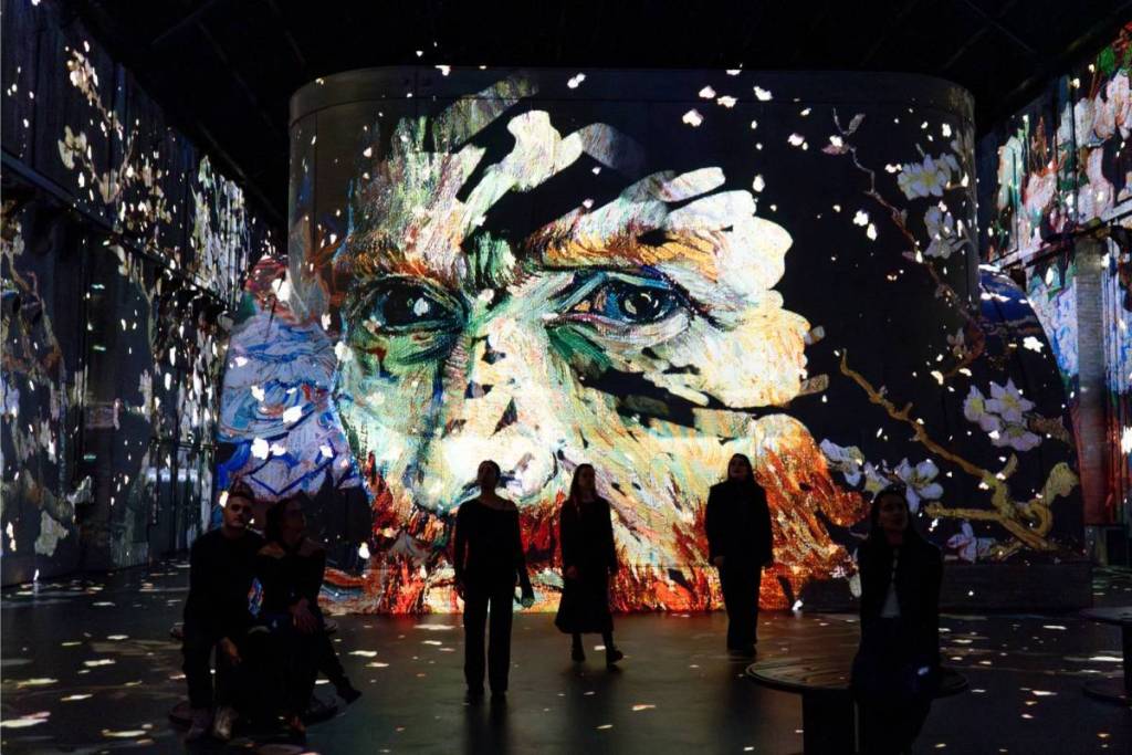An atmospheric and intimate digital art projection featuring a massive close-up of a painted face by Vincent van Gogh on a large central wall.