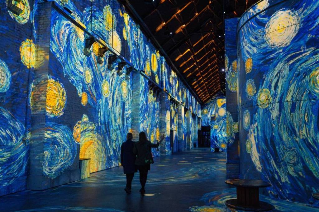 An impressive overview of an elongated, monumental exhibition space completely enveloped in a 360-degree projection of Vincent van Gogh’s “The Starry Night.”