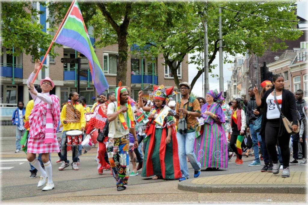 A festive parade of people in colorful, patterned clothing walking through a city street.