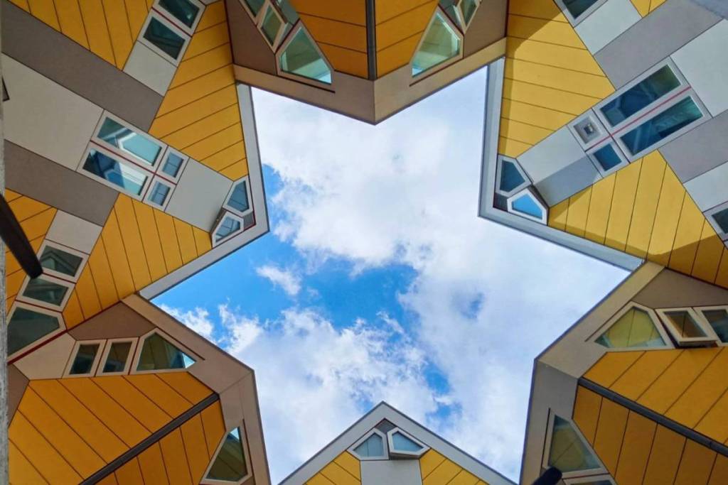 Kikvorsperspectief recht omhoog kijkend naar de gele Kubuswoningen in Rotterdam, waarbij de schuine daken een perfecte ster vormen tegen de blauwe lucht.