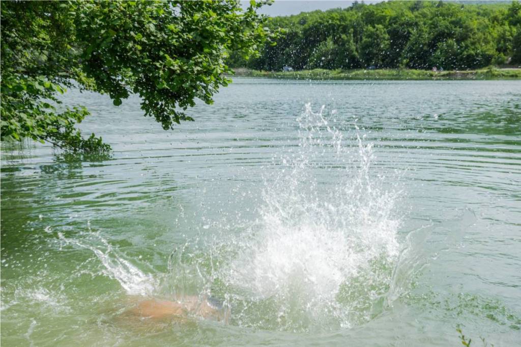 A big splash in a natural recreational lake surrounded by green trees on a hot summer day.