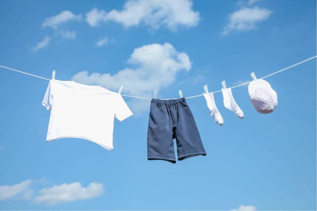 Lightweight clothing, such as a white T-shirt and shorts, hangs on a clothesline to dry under a clear blue sky.