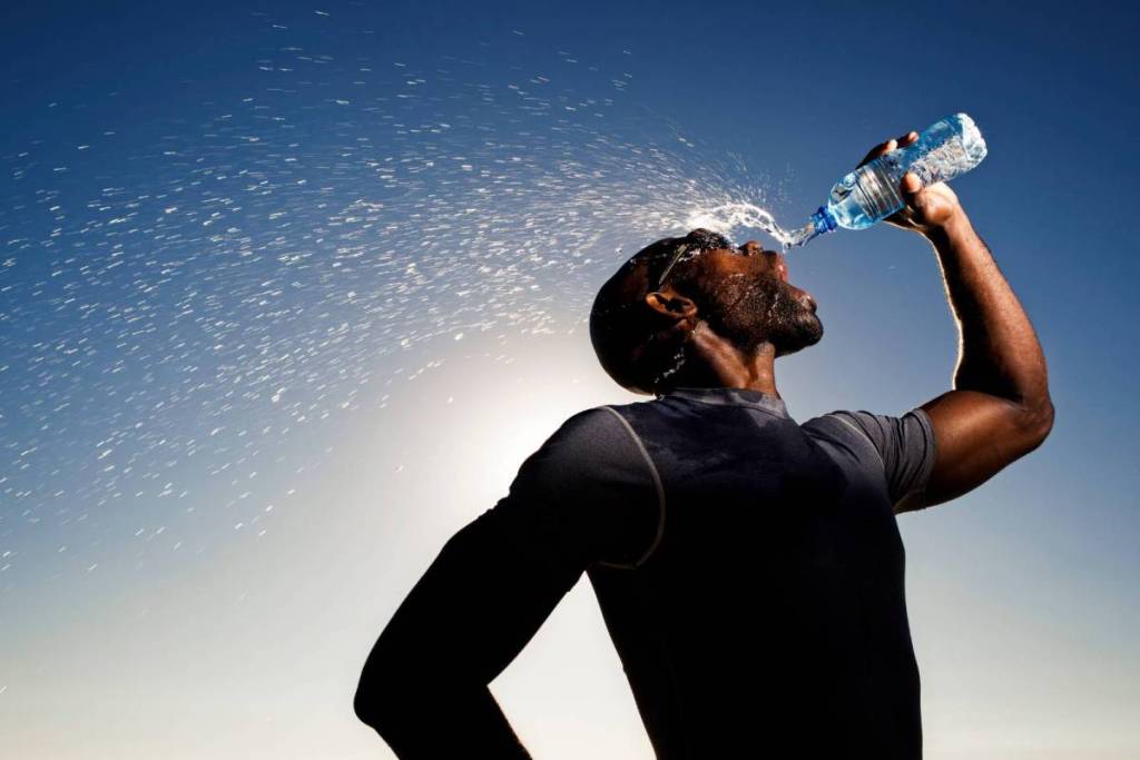 A man drinking from a plastic bottle while splashing water on his face to cool off in the blazing sun.