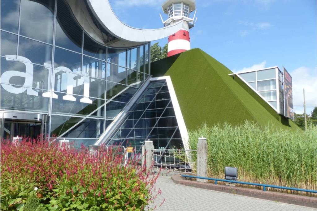 Madurodam’s modern glass entrance, featuring a red-and-white lighthouse rising above the artificial grass roof.