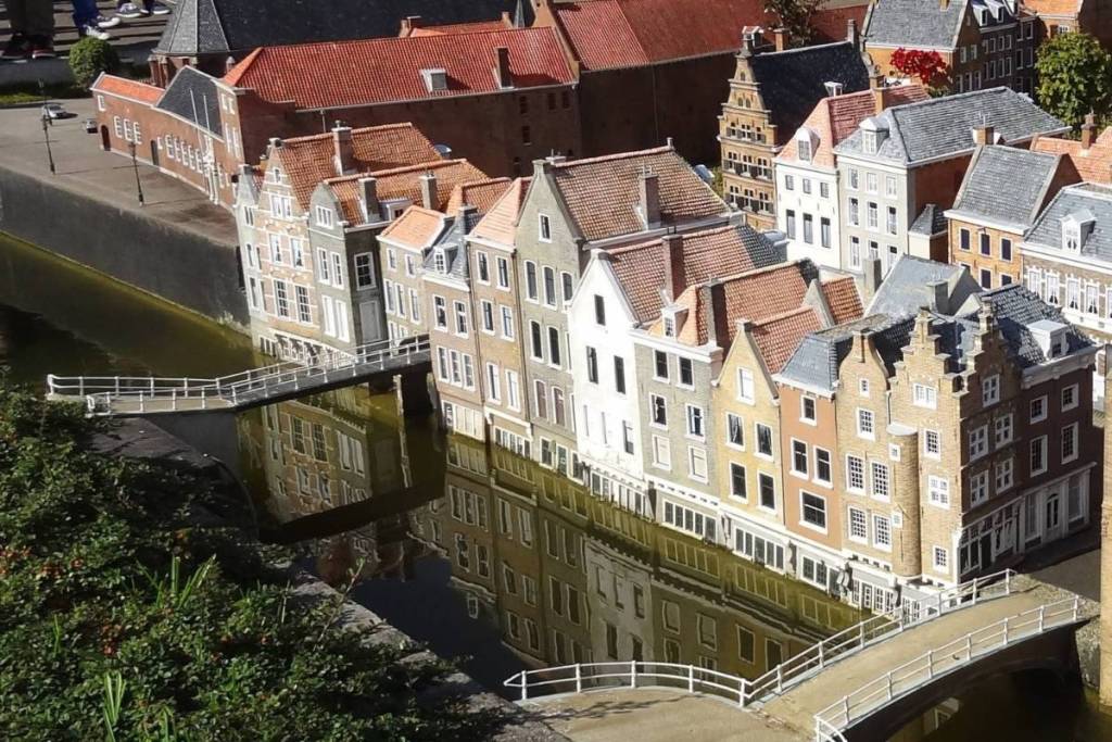 Miniature canal-side buildings and an arch bridge are reflected in the water of a miniature canal in Madurodam.