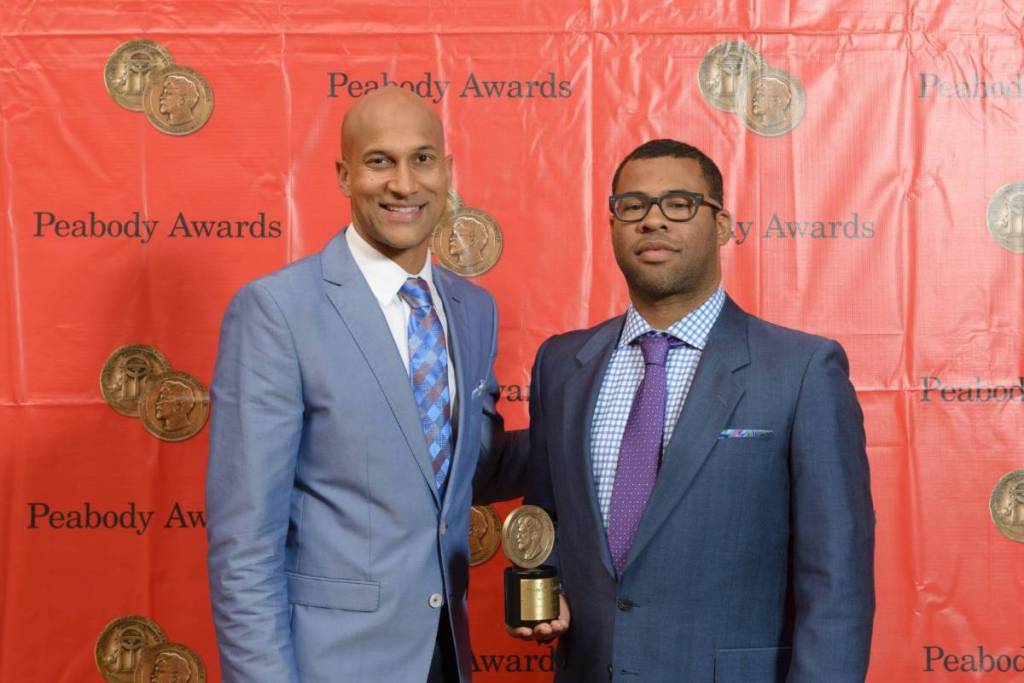 Keegan-Michael Key in een blauw pak en Jordan Peele in een grijs pak poserend met een Peabody Award voor een rode achtergrond.