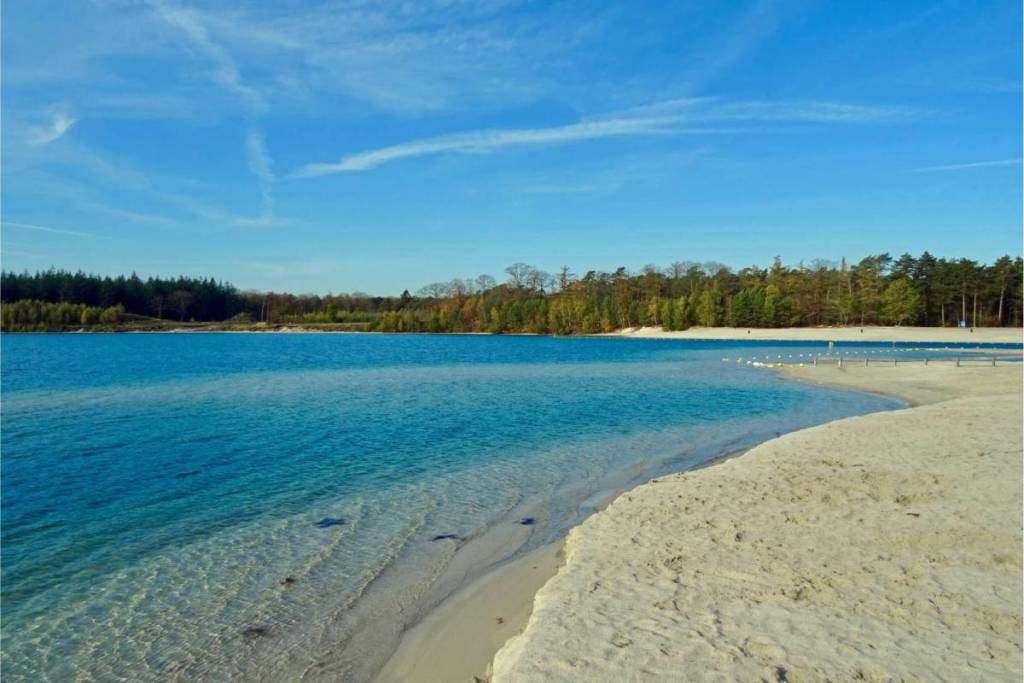 A view of the clear turquoise water and the wide sandy beach of the Gasselterveld, with a dense forest edge in the background.
