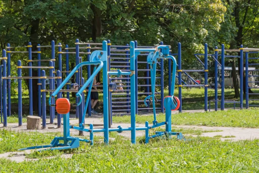 Een gratis calisthenics park in Amsterdam met blauwe fitnesstoestellen en optrekstangen tussen de groene bomen.