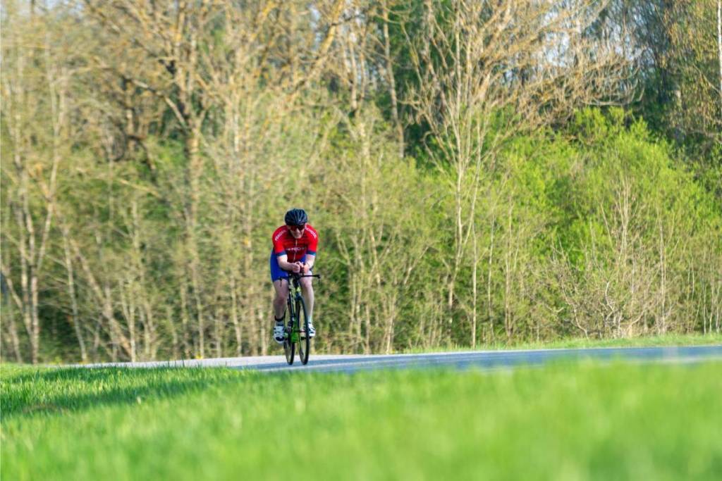 Een wielrenner fietst op een geasfalteerd pad door de groene natuur van het Amsterdamse Bos tijdens een triatloontraining.