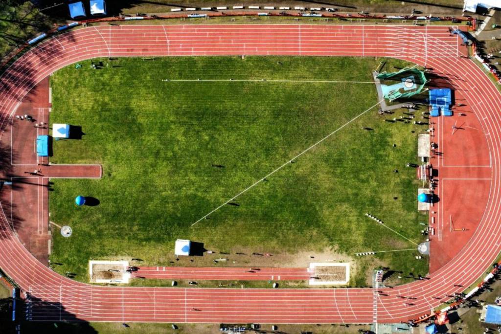 Een luchtfoto van een professionele rode atletiekbaan met witte banen en een groen grasveld voor hardlooptraining