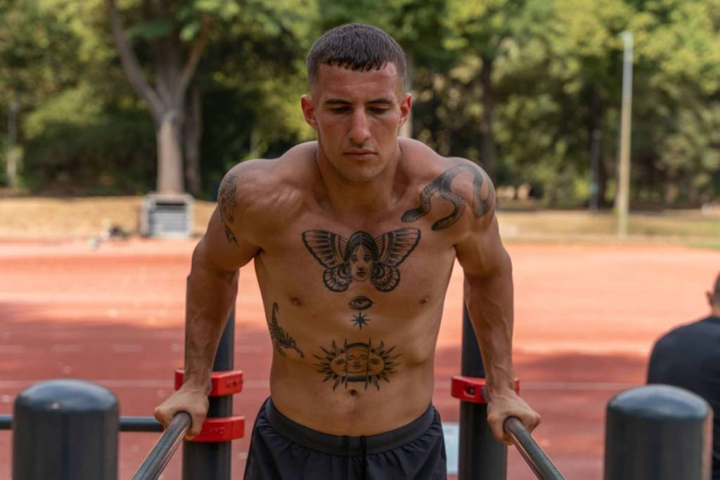 Een gespierde man met tatoeages doet dips op parallel bars tijdens een intensieve calisthenics workout