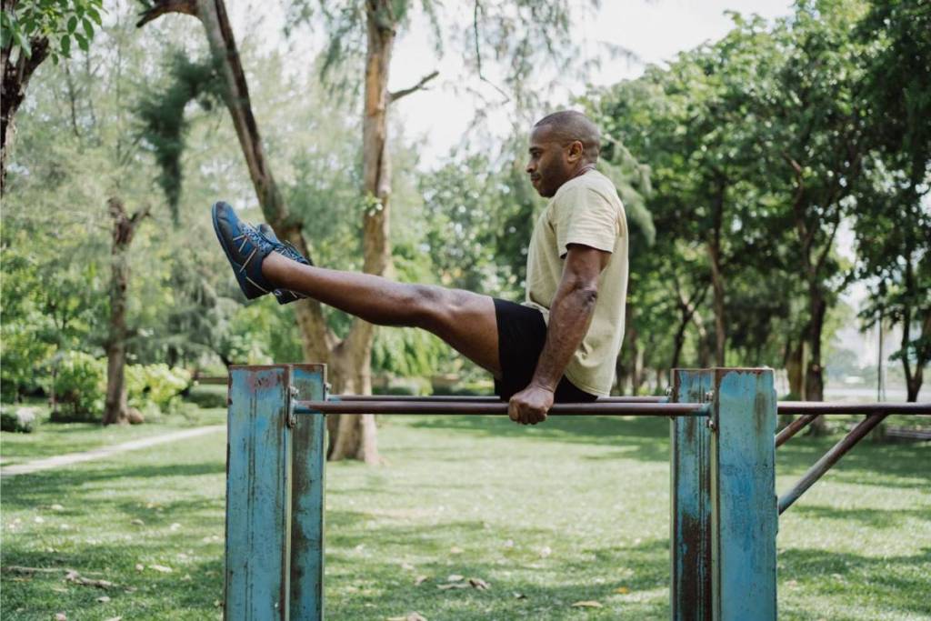 Een man traint zijn buikspieren met een L-sit op de blauwe parallel bars van een buitenfitnesslocatie in Amsterdam.