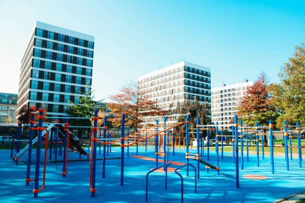 Een modern openbaar calisthenics park in Amsterdam met kleurrijke fitnesstoestellen en een blauw-oranje rubberen ondergrond voor krachttraining.