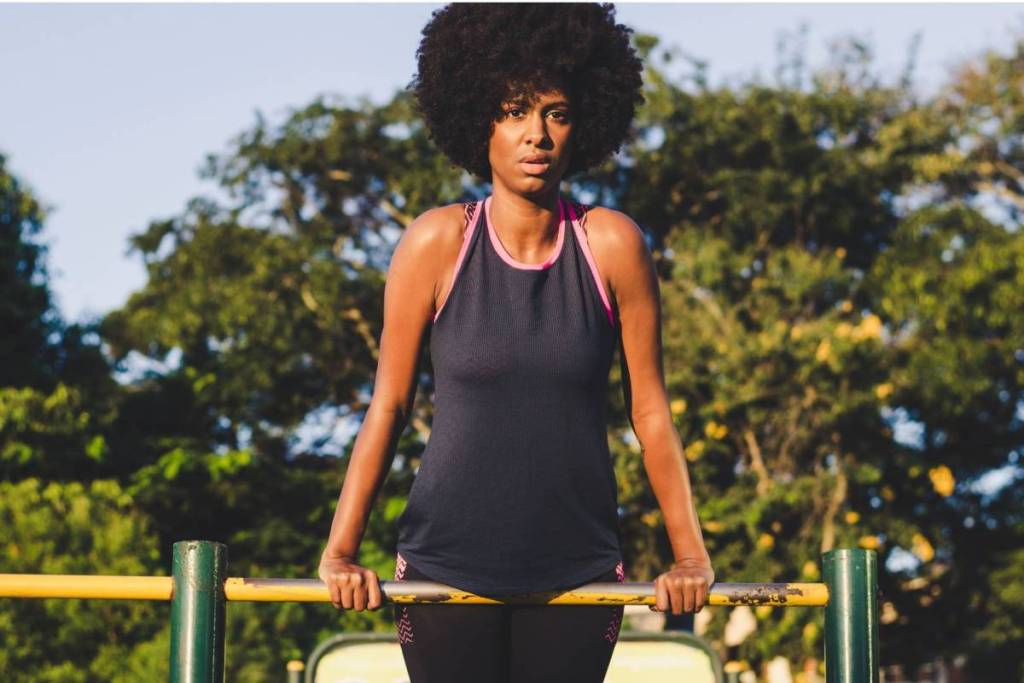 Een gefocuste vrouw met een afro-kapsel traint op een gele optrekstang in een gratis calisthenics park in Amsterdam.
