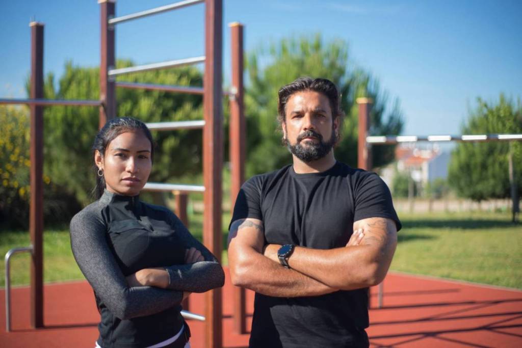 Een sportieve man en vrouw staan met hun armen over elkaar klaar voor een gratis outdoor workout in een Amsterdams calisthenics park.