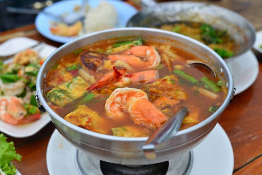 Eine traditionelle Servierplatte aus Metall, gefüllt mit thailändischer Suppe mit Garnelen und Ei, in einem stimmungsvollen Restaurantambiente.