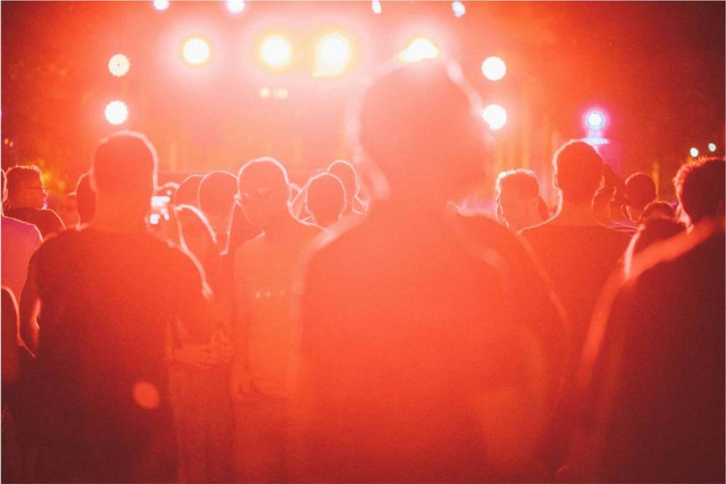 A large crowd of festivalgoers dancing in front of a brightly lit stage with red lights during an open-air concert in Amsterdam