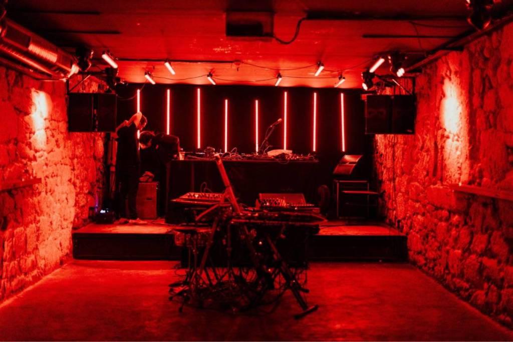 An underground nightclub in Amsterdam with authentic stone walls and bright red neon lights surrounding the DJ booth