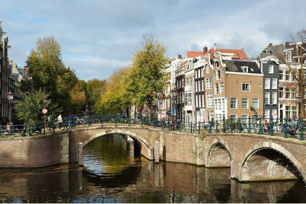 A typical Amsterdam cityscape with historic canal-side buildings and a brick arch bridge full of bicycles spanning the water