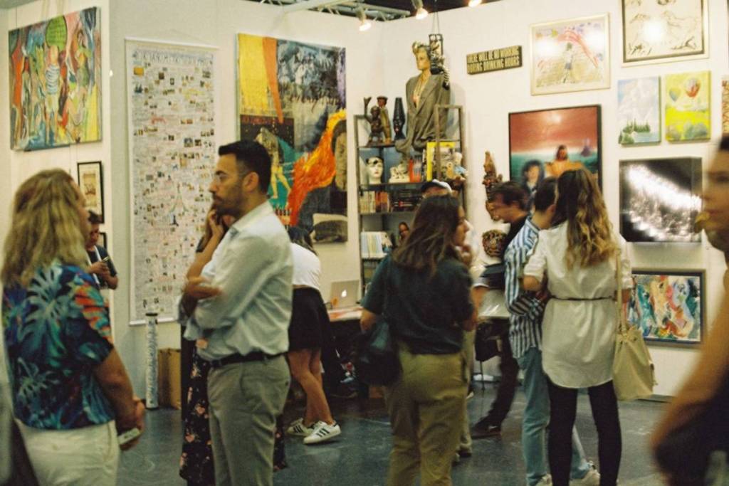 Visitors gathering to view various paintings and modern artworks on the walls of a vibrant art exhibition
