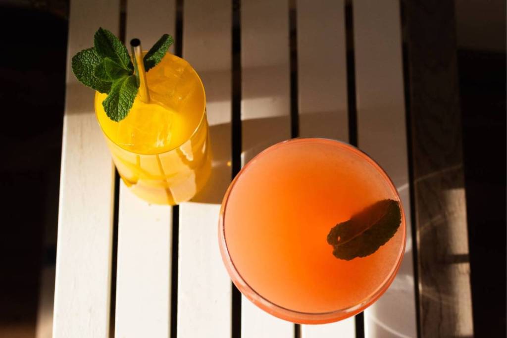 Two colorful summer cocktails with fresh mint leaves, photographed from above on a white wooden table