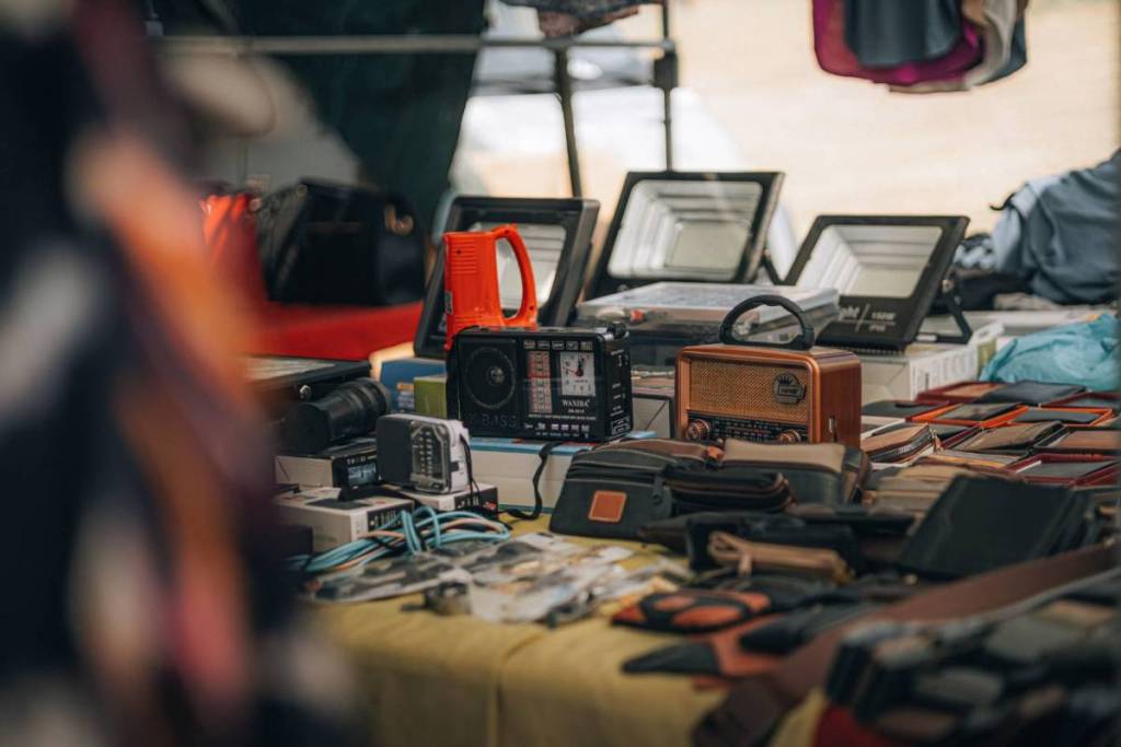 A market stall at a lively flea market in Amsterdam, with vintage radios, leather wallets, and various secondhand electronics displayed on a table
