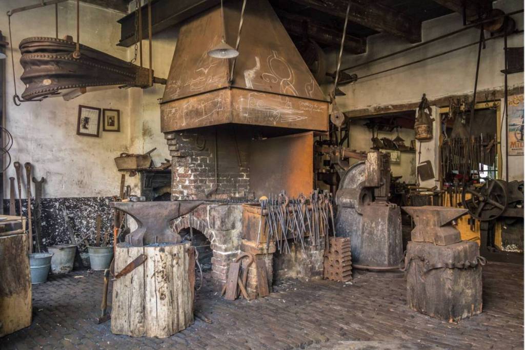 Eine authentische historische Schmiede im Zuiderzeemuseum mit Ambossen, Blasebälgen und Schmiedewerkzeugen auf altmodischem Klinkerboden.