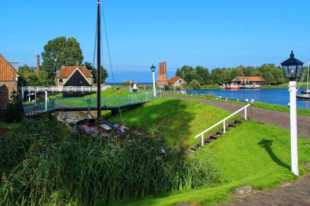 Ein hölzernes Segelboot liegt im Kanal des Freilichtmuseums in Enkhuizen vor Anker, im Hintergrund sind historische Kalköfen zu sehen.